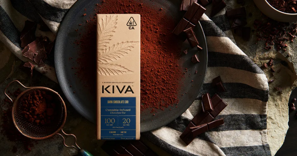 Kiva coffee bag on a patterned cloth with scattered coffee beans and a cup of ground coffee
