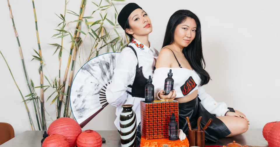 Two women posing indoors with decorative bottles and red lanterns, wearing white and black outfits.