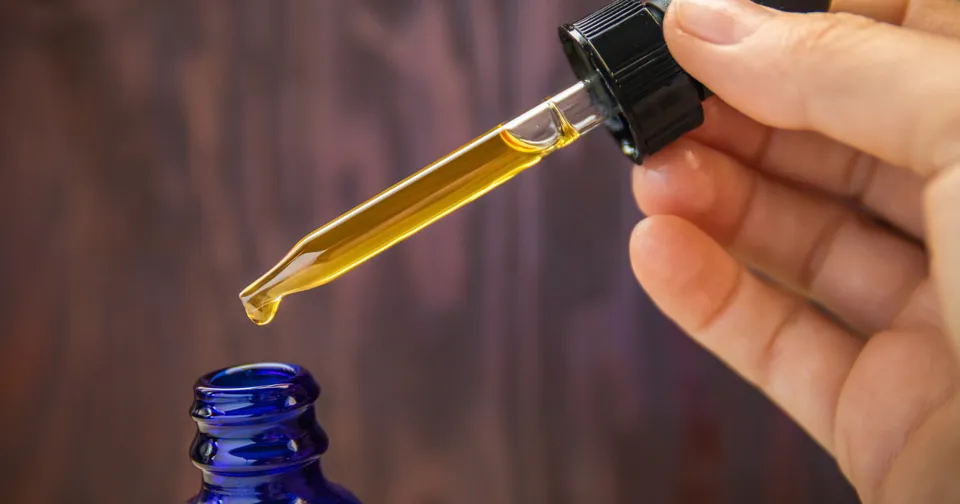 Dropper releasing golden oil into a blue bottle opening