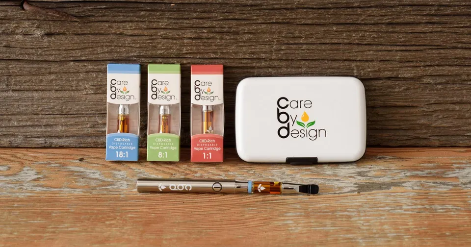 Three CBD oil boxes, a vape pen, and a white case on a wooden table.